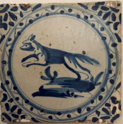 A blue and white hand painted wall tile of a dog rising up on its hind