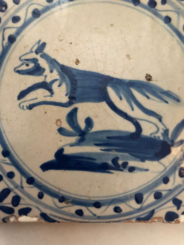 A blue and white hand painted wall tile of a dog rising up on its hind